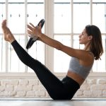 Young woman practicing yoga, Paripurna Navasana exercise with a ring