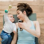 Top view of mother with baby boy lying on floor and playing with dumbbells