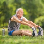 Joyful senior stretching his legs in a park